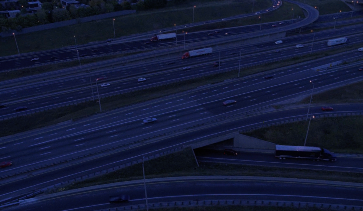 Screenshot from 'Crash': overhead evening shot of cars and trucks zooming over a freeway. 